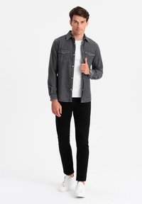 Donkergrijze spijkerblouse met twee borstzakken, knoopsluiting aan de voorkant en een spitse kraag, gedragen met zwarte slim-fit broek en witte sneakers.