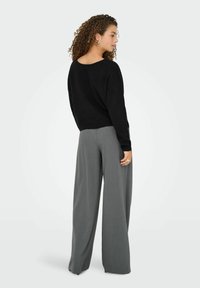 Zwart sweater met een relaxte pasvorm, brede grijze broek met een soepele textuur, met een subtiel patroon. Model staat met de rug naar de camera en toont de outfit.