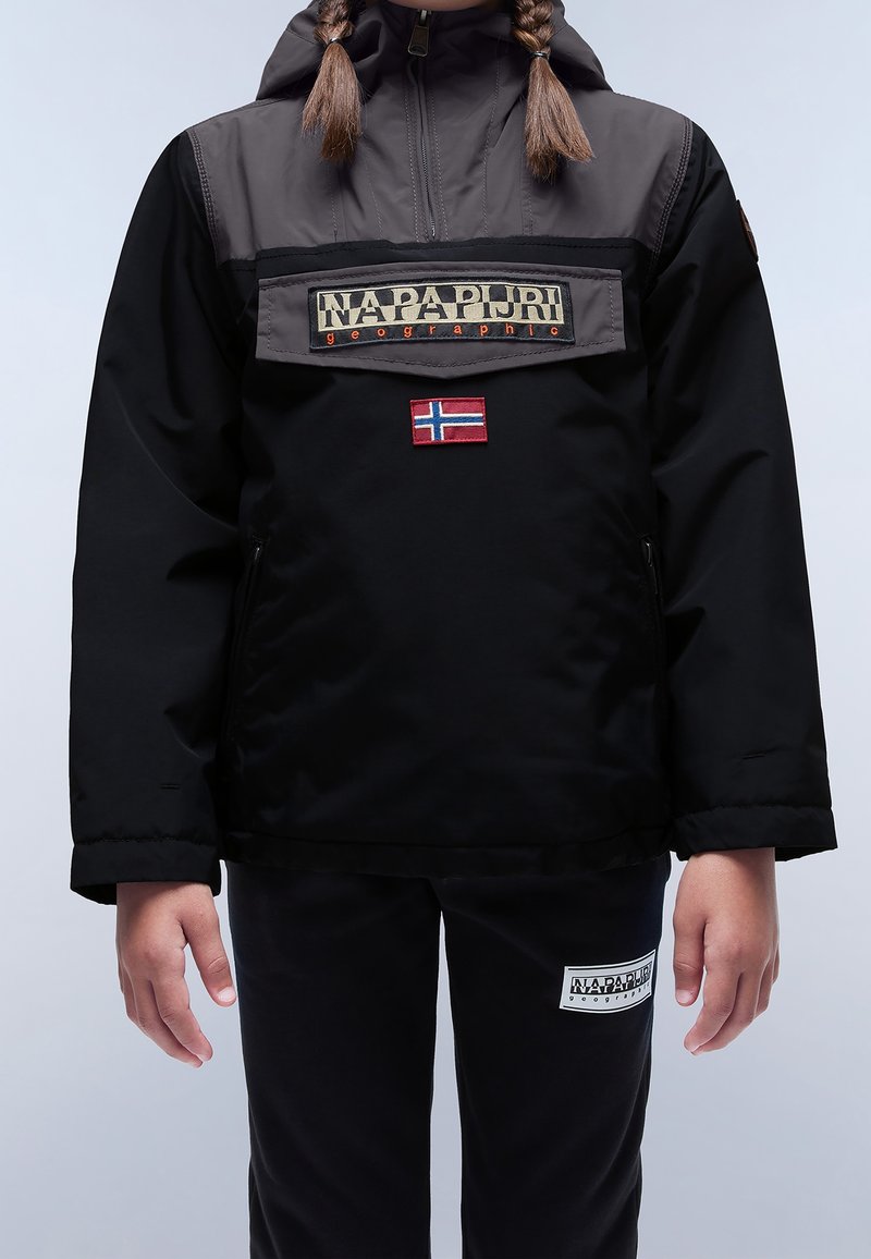 Enfant portant une veste Napapijri noire et grise avec un patch du drapeau norvégien et un pantalon noir avec un patch logo Napapijri.