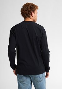 Schwarzes Langarm-T-Shirt aus Baumwolle mit Rundhalsausschnitt und lässigem Schnitt, kombiniert mit hellblauen Denim-Jeans.