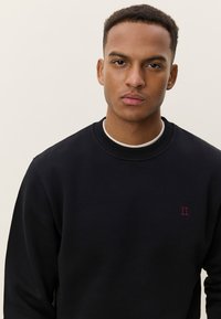 Μαύρο φούτερ με στρογγυλή λαιμόκοψη και ριμπ μανσέτες. Διαθέτει μικρό κόκκινο λογότυπο "II" στο αριστερό στήθος. Λείο ύφασμα.