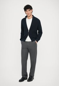 Ναυτικό πλεκτό πουλόβερ με φερμουάρ πάνω από λευκό πουκάμισο, συνδυασμένο με γκρι παντελόνι με σχέδιο και μαύρα παπούτσια. Απλός σχεδιασμός, υφές με υλικά.