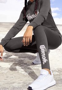 Sweatshirt gris avec logo "Bench", leggings assortis avec impression de logo, chaussures de sport blanches. Tissu lisse, coupe ajustée et accents texturés.