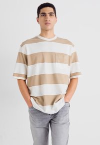 Short-sleeve striped t-shirt in beige and white, featuring a chest pocket and round neckline, paired with light gray jeans.