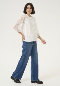 White top with lace 3/4 sleeves, paired with loose blue jeans and black platform shoes. Simple design emphasizes texture and contrast.