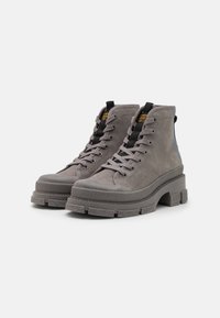 Botas de tobillo de ante gris con suela de goma gruesa, cierre de cordones en la parte delantera y asa de tiro. Presentan acentos texturizados y un diseño de punta redondeada.