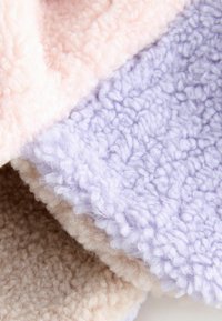 Soft, textured fabric in blush pink, lavender, and beige colors; features a fluffy, cozy appearance with a tactile, fleece-like surface.