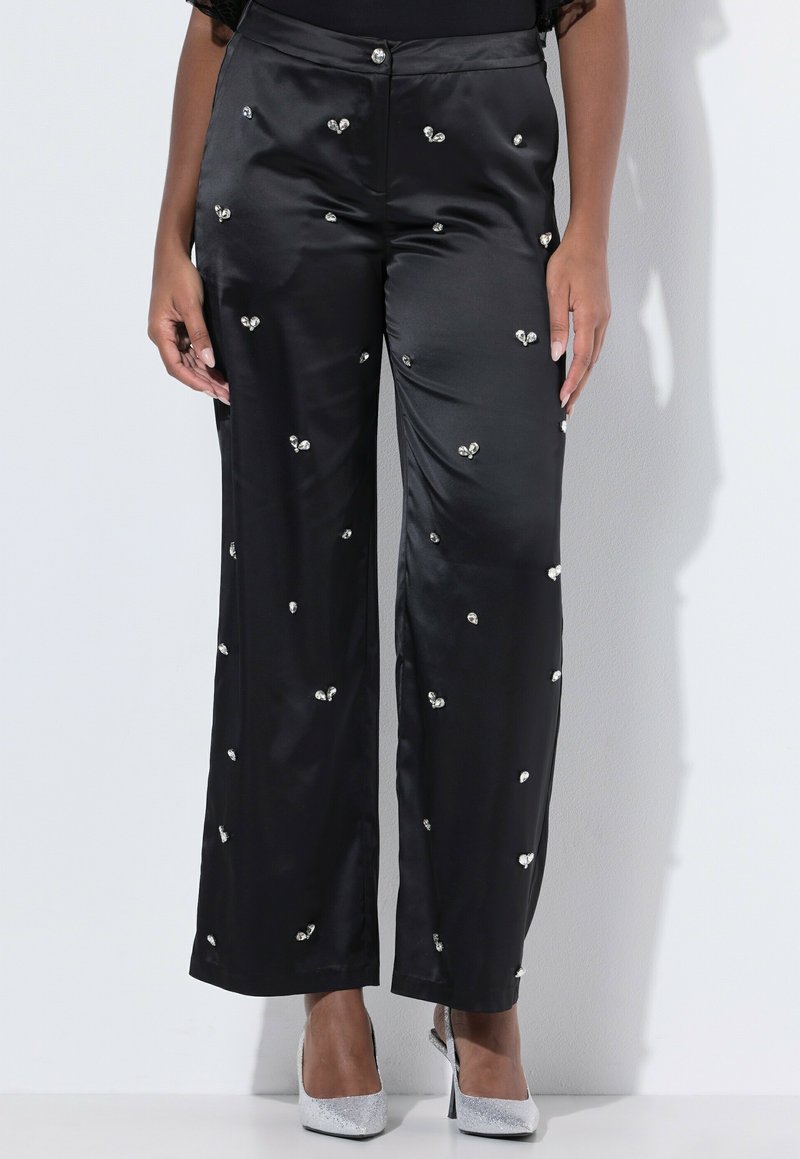 Černé saténové kalhoty s stříbrnými ozdobami, rovného střihu a hladké textury. Styly s stříbrnými vysokými podpatky.