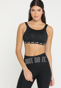 Svart sports-BH med teksturert design og logobånd. Kombinert med svarte høyhårede leggings med "JUST DO IT." i hvit skrift.