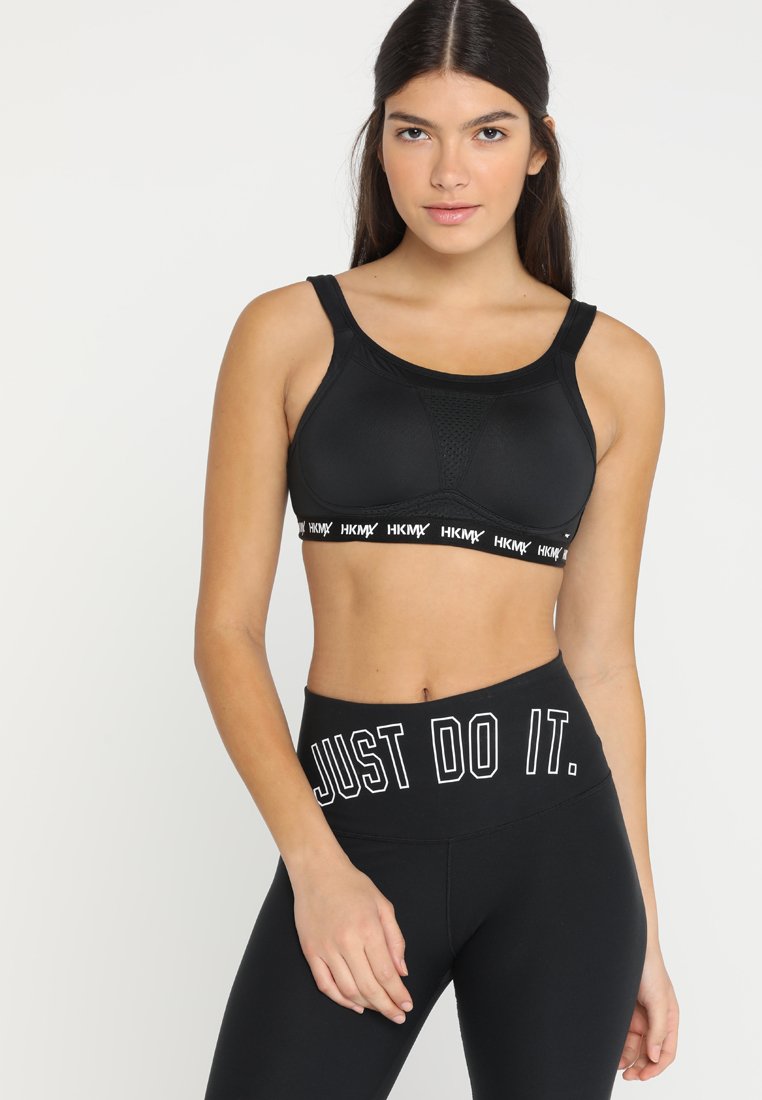 Svart sports-BH med teksturert design og logobånd. Kombinert med svarte høyhårede leggings med "JUST DO IT." i hvit skrift.