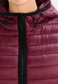 Bordowa kurtka puchowa z kapturem, z pikowaną fakturą, z zamkiem błyskawicznym z przodu i czarnymi akcentami sznurka przy otworze kaptura.
