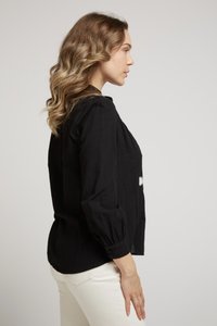 Blouse noire légère avec coupe ample, manches bouffantes longues et poignets boutonnés. La texture du tissu semble légèrement froissée. Design simple.