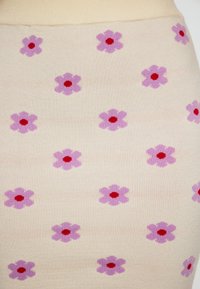 Knie-langer hellbeiger Rock mit einem gerippten Bund, der ein wiederholtes Muster aus lila Blumen mit roten Zentren aufweist. Glatte Stofftextur.