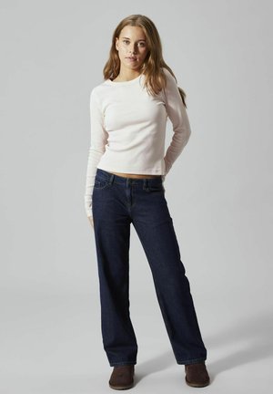 Helles rosa Langarmoberteil mit rundem Halsausschnitt, kombiniert mit dunkelblauen weiten Jeans und braunen Ankle Boots. Einfaches, lässiges Outfit.