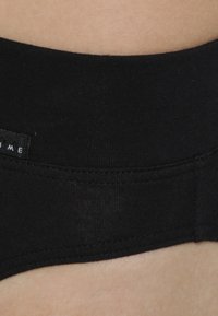 Zwarte katoenen tailleband met een gladde textuur, voorzien van een eenvoudig ontwerp en een naadloze afwerking. Kleine logo-detail zichtbaar op de rand.