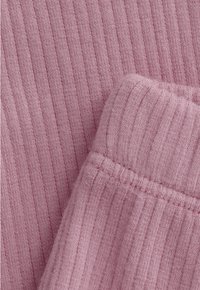 Nahaufnahme von weichem, geripptem Strickstoff in hellem Mauve mit sichtbaren Nahtdetails an der gefalteten Kante.