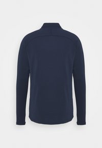 Granatowy polo z długim rękawem, kołnierzykiem, gładką fakturą i subtelnymi przeszyciami na ramionach. Brak widocznych logo lub wzorów.