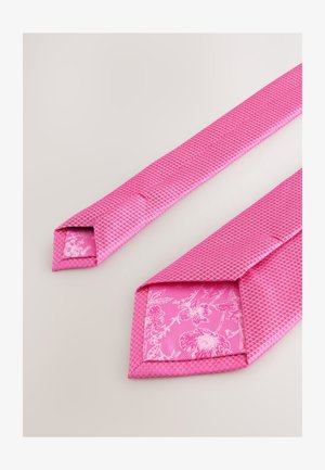 Rožinės spalvos tekstūruota kaklaraištis su tinklelio raštu, po apačia puošta gėlių motyvais. Dizainą užbaigia smailūs galiukai ir lygus paviršius.