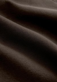 Tessuto marrone scuro con una texture liscia, che mostra pieghe e grinze morbide, realizzato in una miscela di cotone a peso medio.