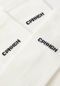 Calcetines blancos con textura acanalada que presentan el texto bordado en negro "CRUNCH" en el lateral. Altura estándar de caña, textura suave y ajuste ceñido.