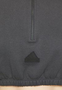 Mörkgrå träningshuvtröja med dragkedja, ribbat avslut och en texturerad svart Adidas-logotyp i nedersta vänstra hörnet.