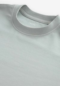 Tricou din bumbac gri deschis, cu decolteu rotund și guler ribbit. Materialul pare neted și ușor texturat. Eticheta este vizibilă în interior.