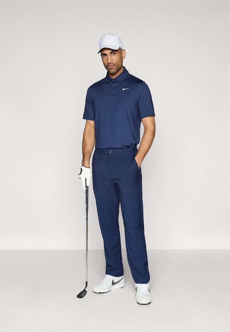 Marineblaues Polo- und Hosen-Set mit kragenförmigem Design, glattem Stoff und Nike-Logo. Eine weiße Kappe und Schuhe runden die Golfausstattung ab.