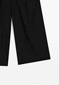 Pantalon noir à jambes larges en tissu subtilement texturé, présenté à plat avec des jambes légèrement froissées sur fond blanc.