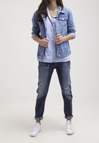 Vaate denim takki vaaleansinisenä, päällä vaaleansinen paita. Tummansiniset farkut, joissa lahkeet käännetty. Valkoiset lenkkarit täydentävät asun.