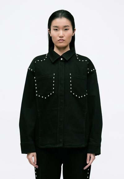 Black denim jacket featuring studded accents along the shoulders and pockets, with a pointed collar and button closure.