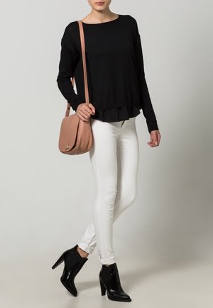 Czarna bluzka z długim rękawem i falbaną na dole, zestawiona z białymi wąskimi jeansami i czarnymi botkami za kostkę. Jasnoróżowa torebka na ramię dodaje kontrastu.