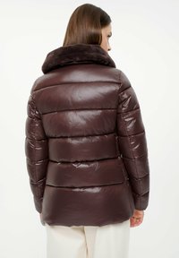 Brązowa kurtka puchowa o połyskującym wykończeniu, z pluszowym, ciemnym futrzanym kołnierzem i poziomym pikowaniem zapewniającym izolację i ciepło.