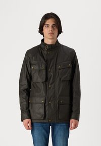 Veste en coton ciré vert olive avec un col haut, quatre poches avant et des boutons en laiton. Dispose d'accentuations aux épaules et d'une coupe ajustée.