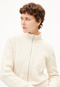 Weißer gerippter Strickpullover mit hohem Kragen und Reißverschluss. Verfügt über lange Ärmel und strukturierten Stoff. Einfaches und minimalistische Design.