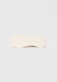 Sole of a light-colored sneaker; textured rubber material with a rounded shape and a logo embossed in the center. Smooth, flexible design.