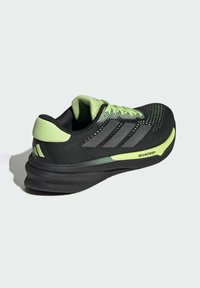 Zapatilla deportiva negra con acentos verdes y parte superior texturizada. Presenta un destacado logotipo de tres franjas y una suela acolchada. Etiqueta Dreamstrike visible.