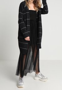 Černý cardigan s bílými pruhy, zkombinovaný s černou síťovanou sukni. Nosený s světlými teniskami. Měkká tkanina, otevřený přední design.