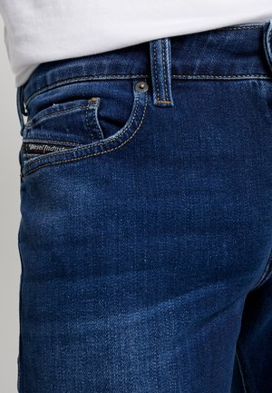 Gros plan d'une poche de jean en denim bleu foncé avec des coutures visibles et une petite étiquette noire indiquant Diesel Industry.