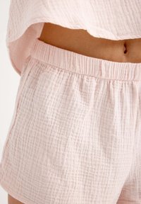 Bermudas de algodón de color rosa claro con un diseño texturizado y arrugado, y una cinturilla elástica. La tela parece suave y transpirable.
