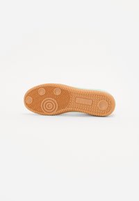 Rubber sneaker sole with a textured, patterned surface in light brown. Features circular and diamond-shaped treads for traction.