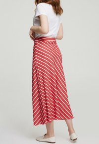 Jupe maxi à rayures rouges et blanches avec un design fluide, fabriquée en matériau léger, présentant une taille haute et une fente sur le côté.