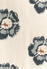 Blommönstrad tyg med en krämfärgad bakgrund som har mörk teal-färgad blommor och mjuka bruna mittpunkter. Slät textur med ett naturligt, vävt utseende.