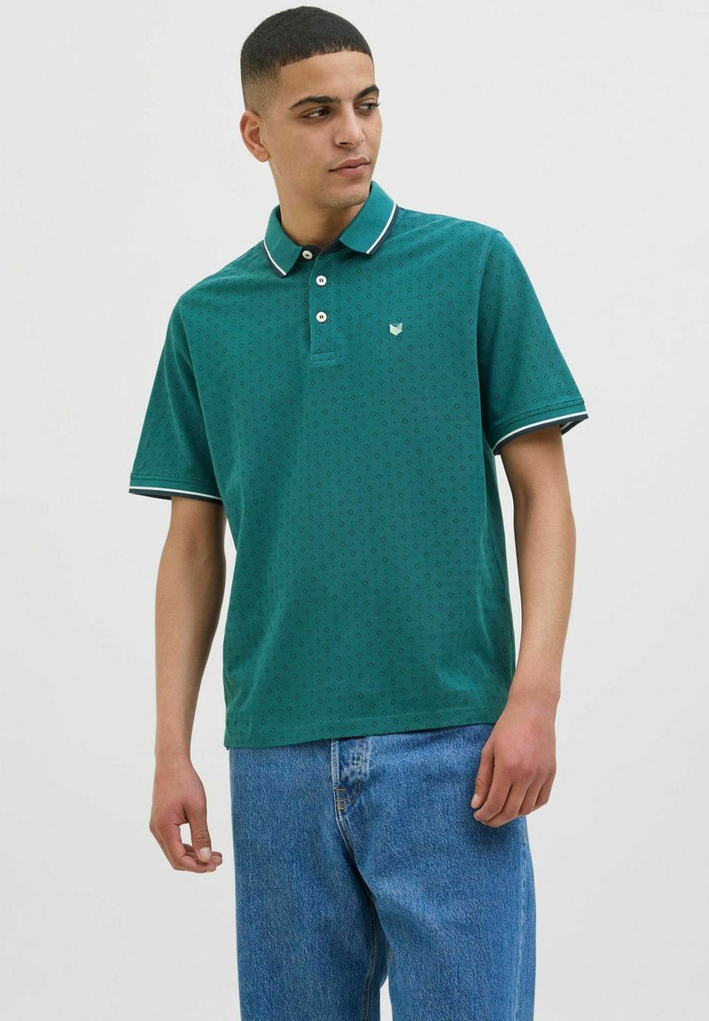 Polo de culoare teal cu o textură modelată, accente albe pe guler și pe manșete, având un mic logo pe piept. Purtați cu blugi albaștri.