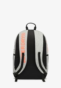 Mochila gris y negra con correas acolchadas que presentan el texto naranja "SUPERDRY", asa superior y extremos de correas ajustables, vista desde la parte de atrás.