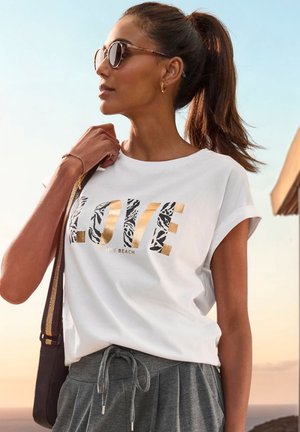 White cotton t-shirt with "LOVE" in gold and animal print, paired with gray drawstring pants. Accented with round sunglasses and a bag.