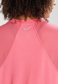 Rosa sporttröja med en slät tygkvalitet och nätstruktur på axlarna och ryggen, prydd med en liten silverfärgad Nike-logotyp.