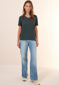 T-shirt verde scuro a V, maniche corte, abbinato a jeans a palazzo blu chiaro e sneakers beige. Tessuto morbido con una vestibilità rilassata.