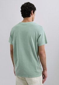 Camiseta de algodón verde claro con mangas cortas, cuello redondo y corte relajado. Textura suave y sutiles detalles de costura.