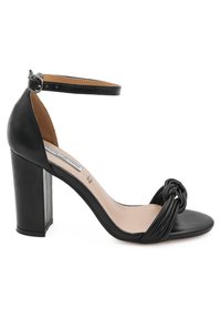 Sandali con tacco alto in pelle nera, con punta arrotondata, dettaglio anteriore annodato e cinturino alla caviglia regolabile. Design con tacco spesso.