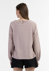 Løs pasform, langærmet bluse i blødt mauve stof. Har en nøglehul i ryggen med knapdetalje, subtil tekstur og raglanærmer.